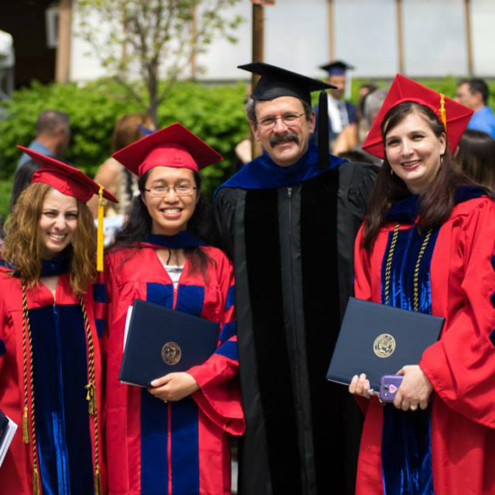 PhD students in graduation gowns with faculty member